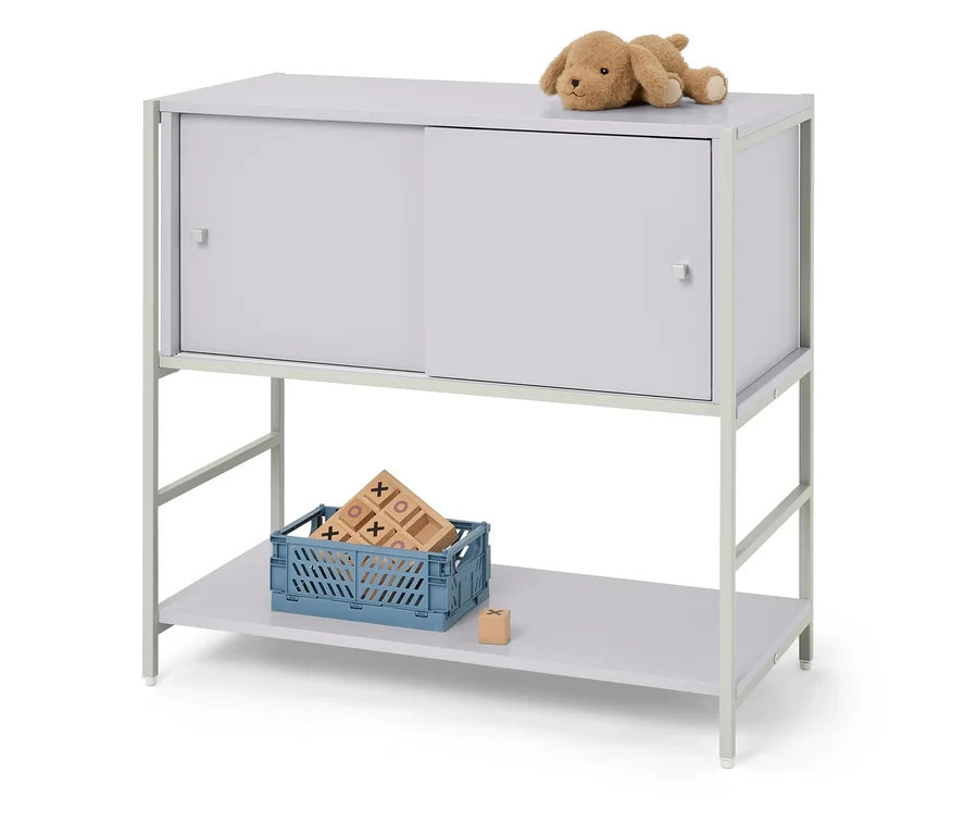 Ein beiger Stoffhund liegt auf einem grauen Schrank mit Schiebetüren. Unter dem Schrank steht eine blaue Kiste mit Holzspielzeug.