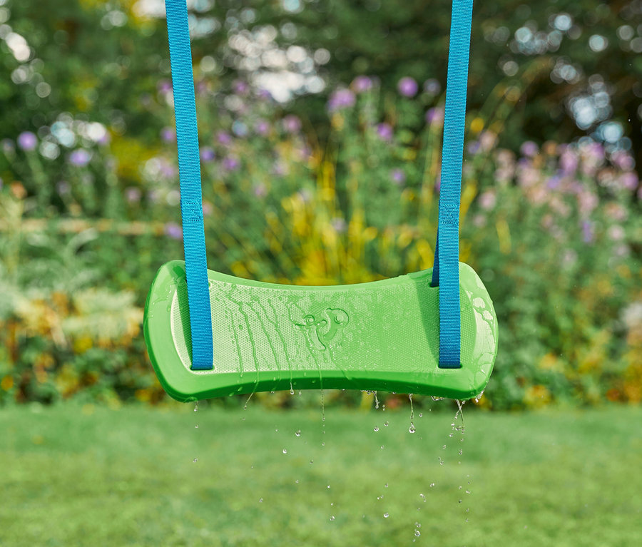 Grüne Schaukel des Kletterturms »Explorer« hängt an blauen Bändern vor Garten.