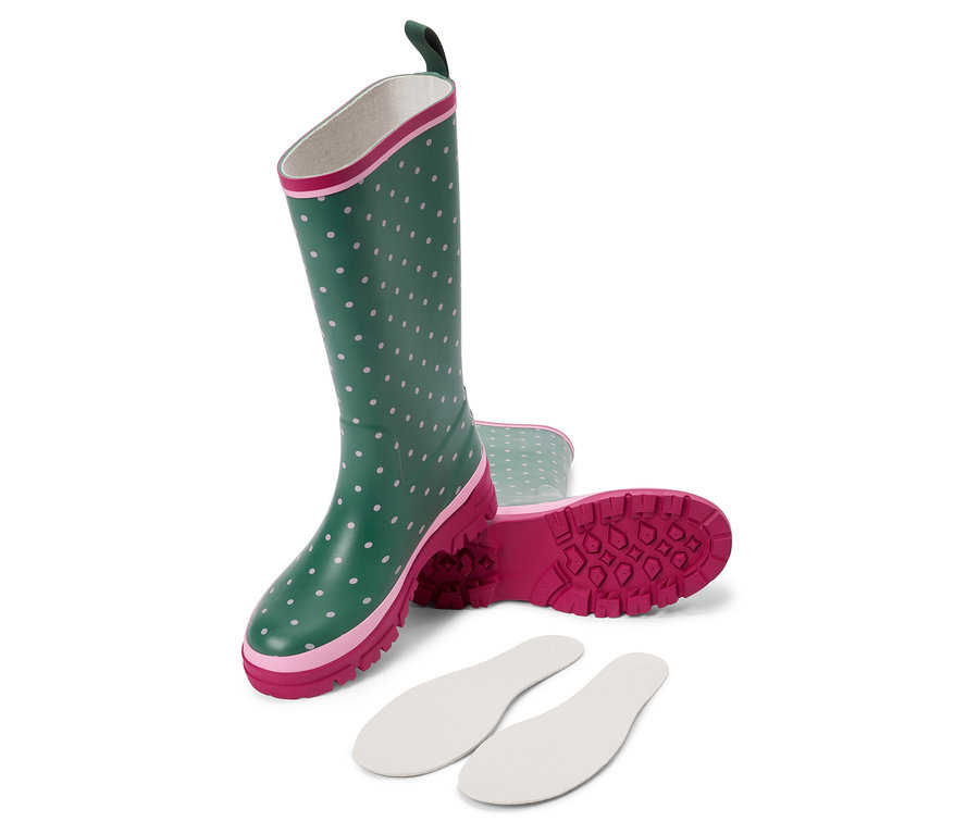 Ein Paar grüne Gummistiefel mit weißen Punkten liegen auf der Seite, daneben liegen weiße Einlegesohlen.