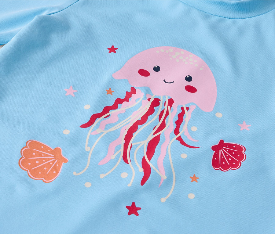 Detailansicht eines hellblauen Stoffes mit einem rosa Quallenaufdruck, umgeben von Muscheln und Seesternen.