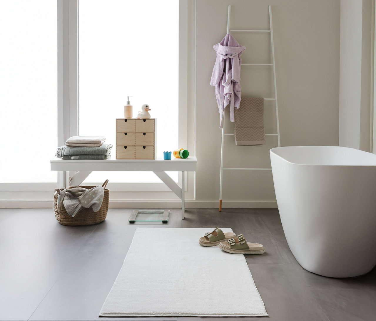 Ein Badezimmer mit einer weißen benuta Badematte »Ole«, 70 x 120 cm, cream, einem weißen Hocker, einer Leiter und einer Badewanne.