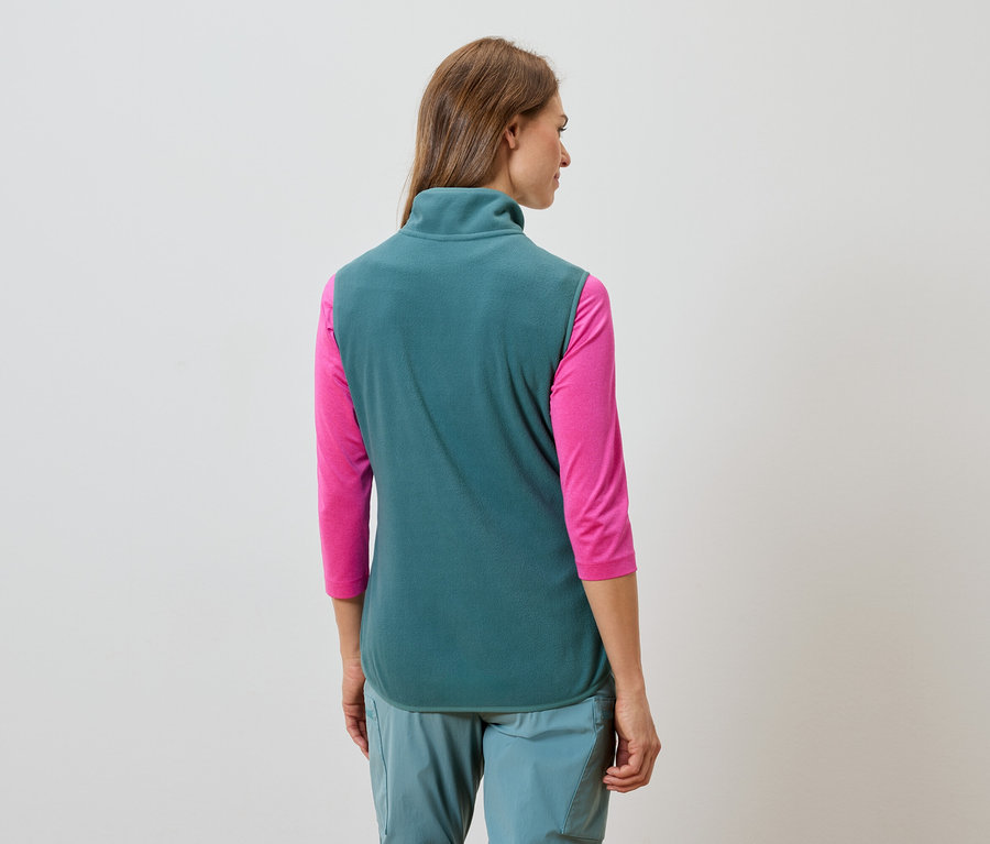 Rückansicht einer Frau mit langen braunen Haaren, die eine türkisfarbene Fleeceweste, ein pinkfarbenes Langarmshirt und türkisfarbene Hosen trägt.
