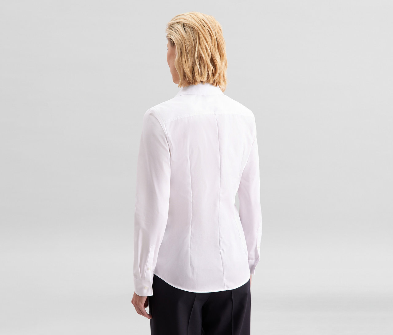 Frau von hinten, trägt eine weiße Seidensticker Bluse Slim Fit non iron und eine schwarze Hose.