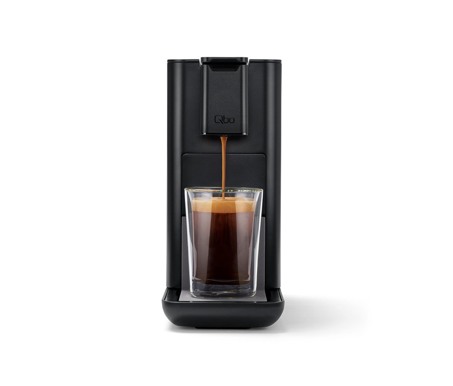 Kaffee fließt aus der Qbo ICONIC Dark Chrome Kaffeemaschine in ein Glas.