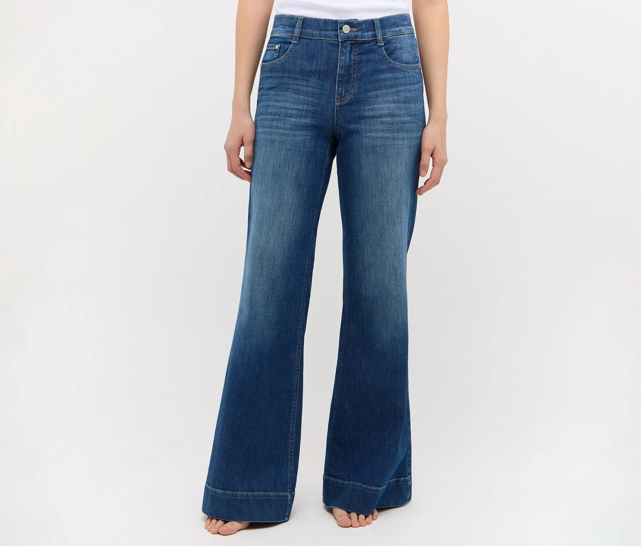 Person trägt blaue, hochgeschnittene Jeans mit weitem Bein und ausgestellten Beinabschlüssen, barfuß stehend.