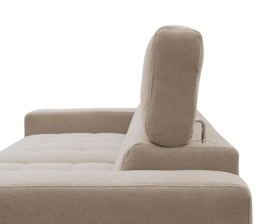 Nahaufnahme einer beigen Couch von der Seite, mit einer gesteppten Sitzfläche, einer breiten Armlehne und einer verstellbaren Kopfstütze, die von einer silbernen Metallstange gehalten wird.