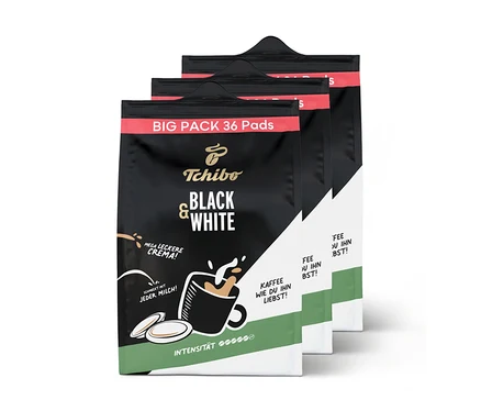 Drei Packungen Tchibo BLACK & WHITE Pads, die vorderste Packung zeigt den Namen und eine Tasse Kaffee mit Milchschaum.