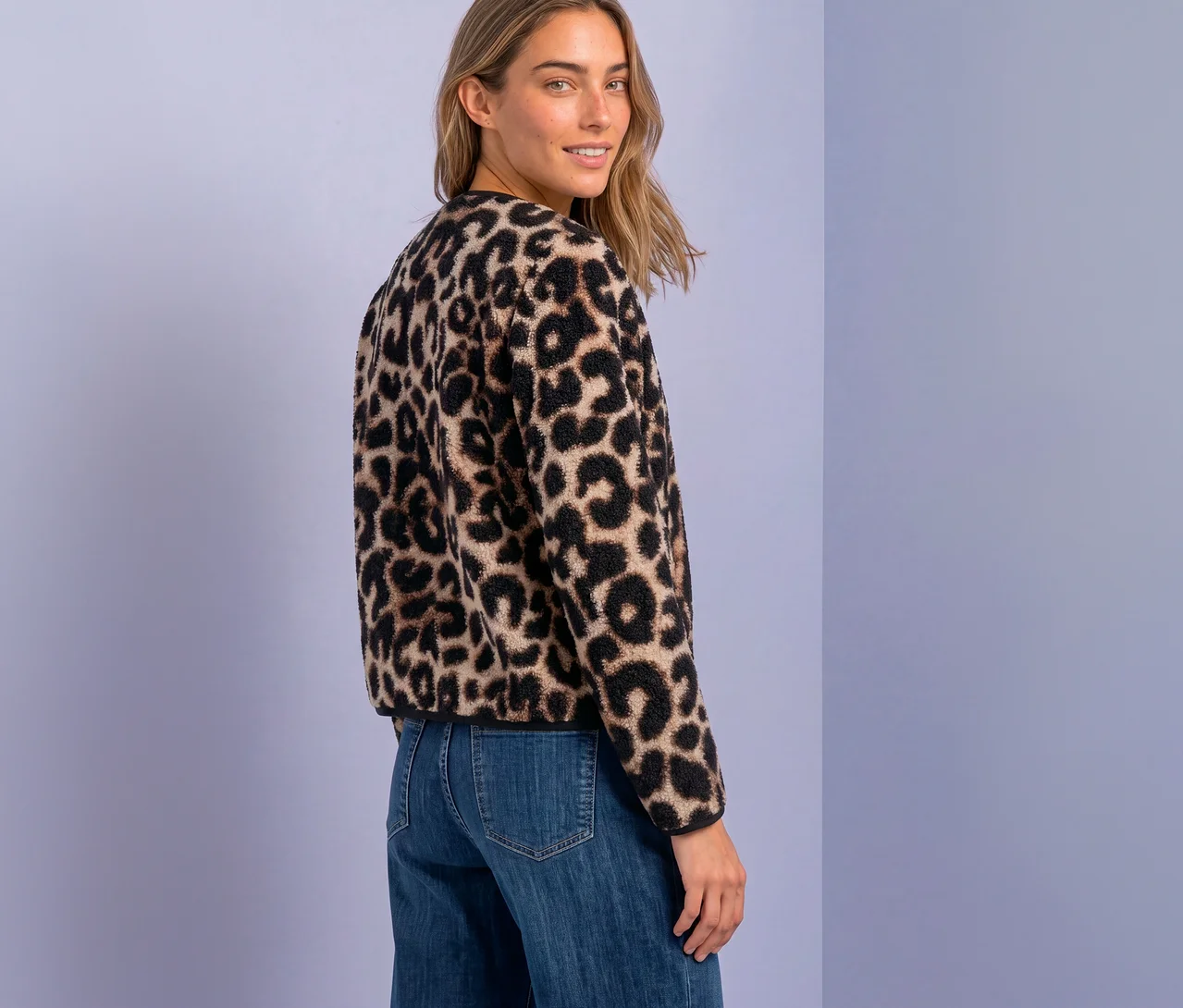 Eine lächelnde Frau mit blondem Haar blickt über ihre Schulter, trägt eine Street One Jacke mit Leopardenmuster und blaue Jeans.