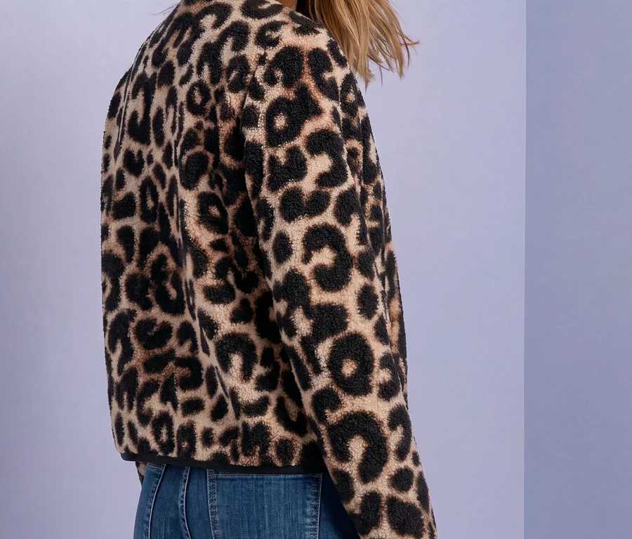 Lächelnde Frau trägt eine Street One Jacke mit Leopardenmuster aus Fleece und blaue Jeans, blickt über ihre Schulter zurück.