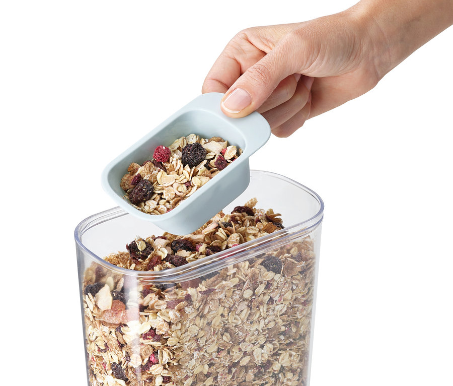 Eine Hand schöpft Müsli mit einem Messlöffel aus einem durchsichtigen Joseph Joseph Aufbewahrungsbehälter-Set.