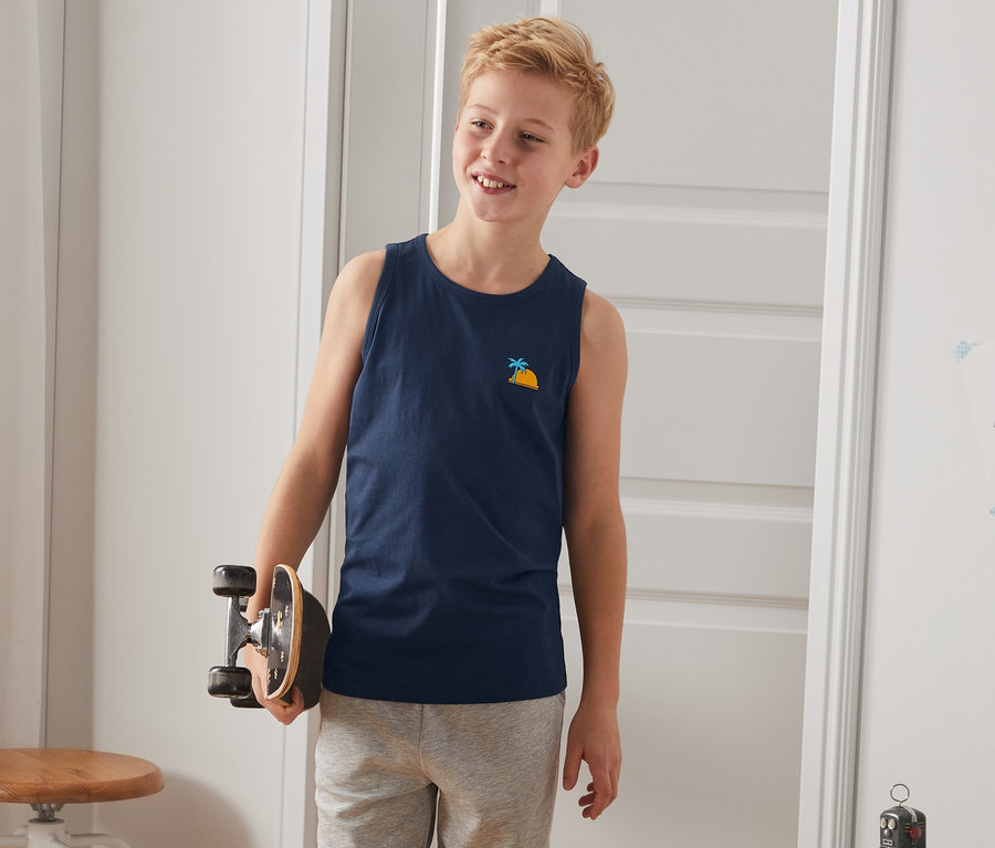 Junge hält Skateboard und trägt 2 Tanktops.