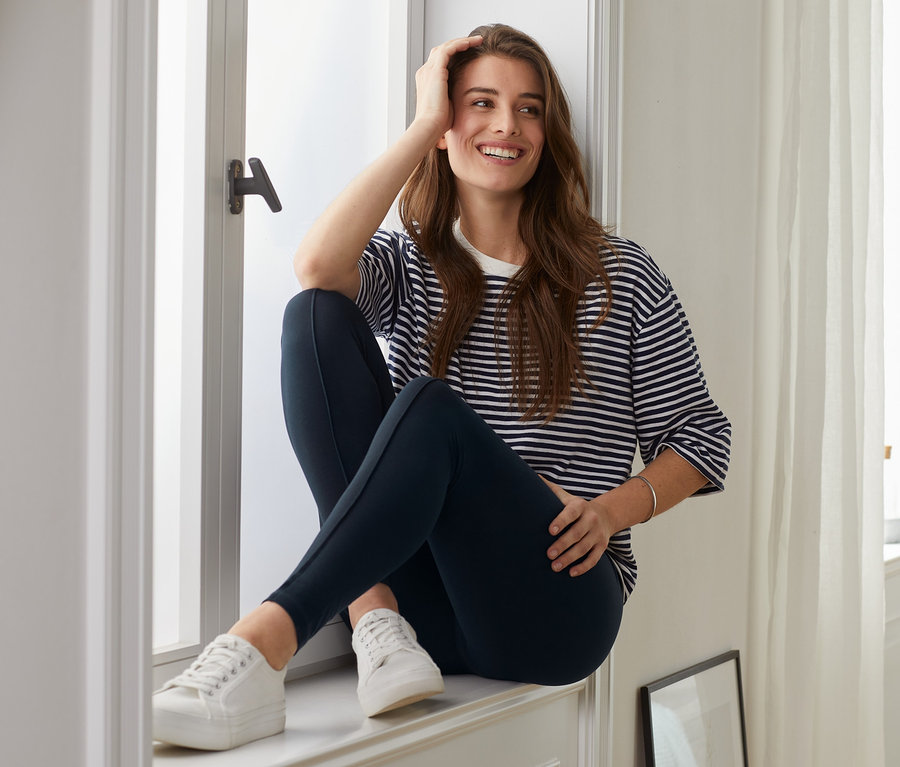 Frau sitzt im Fenster in marineblauen Leggings mit Biese und einem gestreiften T-Shirt.