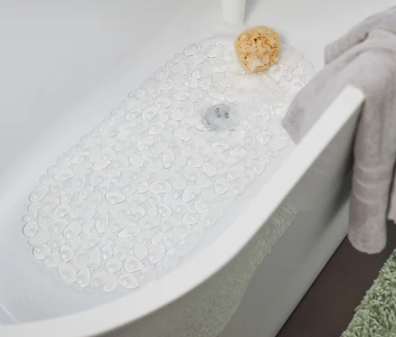 In der Badewanne liegt eine transparente Badewanneneinlage. Ein graues Handtuch hängt am Rand der Badewanne und ein grüner Teppich liegt neben der Badewanne.