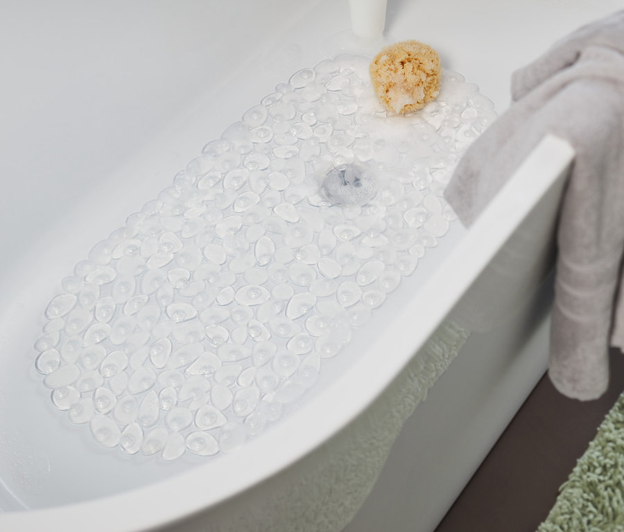 In der Badewanne liegt eine transparente Badewanneneinlage. Ein graues Handtuch hängt am Rand der Badewanne und ein grüner Teppich liegt neben der Badewanne.
