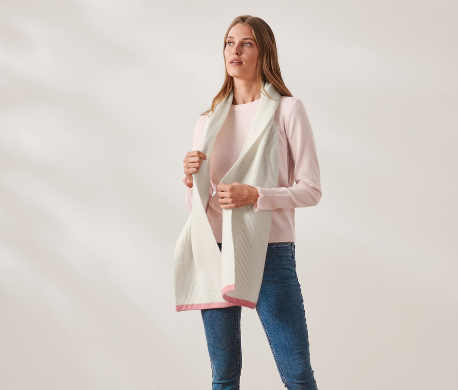 Frau hält einen Strickschal mit Wolle in Creme mit pinkfarbenen Enden.