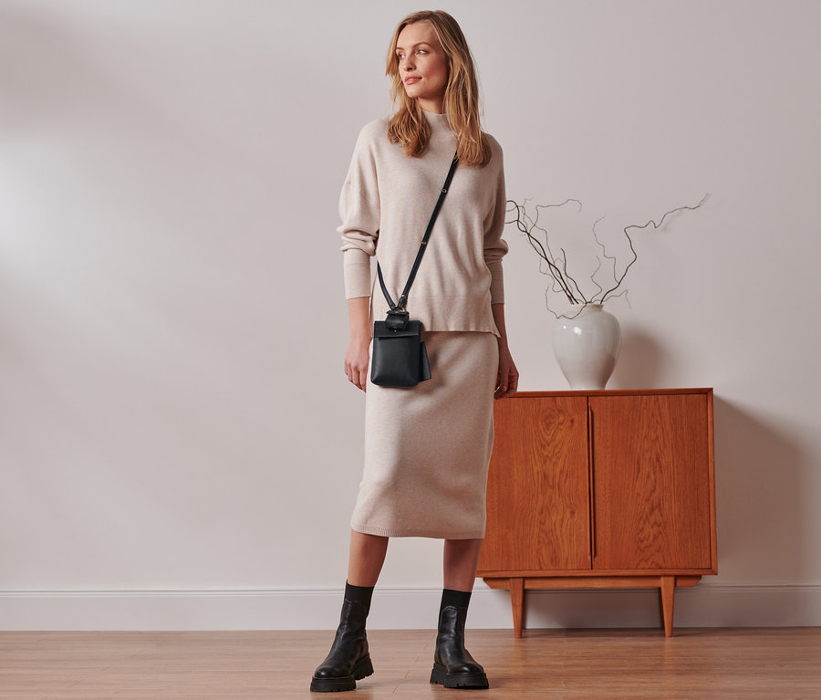 Frau steht im Raum und trägt eine Mini-Tasche.