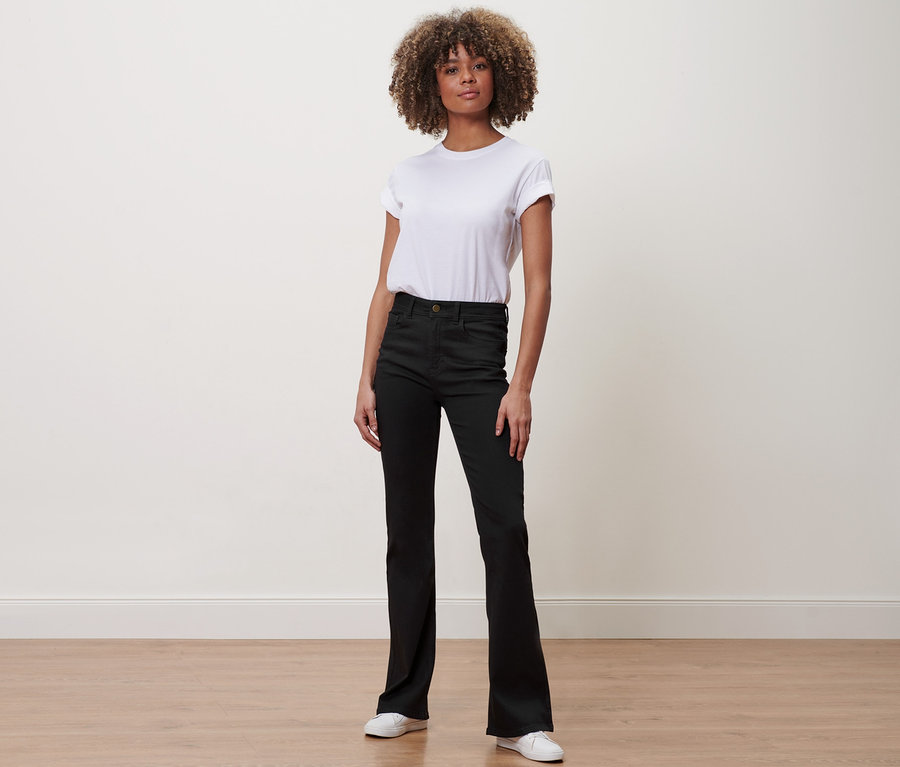 Frau mit Afro steht in Bootcut Denim – Fit Jola und weißem T-Shirt.