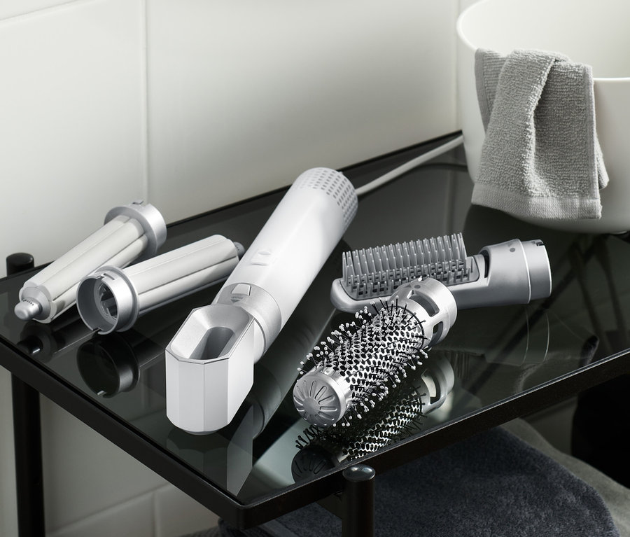 Auf einem gläsernen Badregal liegen ein 5-in-1-Multi-Haarstyler-Set und seine Aufsätze.