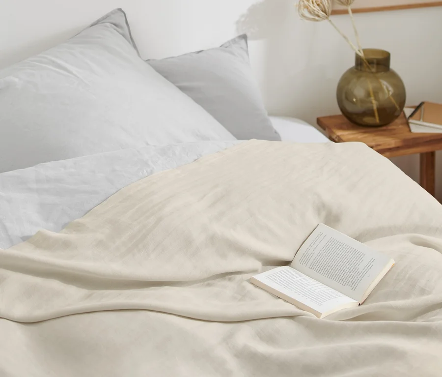 Beiger Überwurf aus gewaschenem Leinen liegt auf einem Bett mit einem offenen Buch.