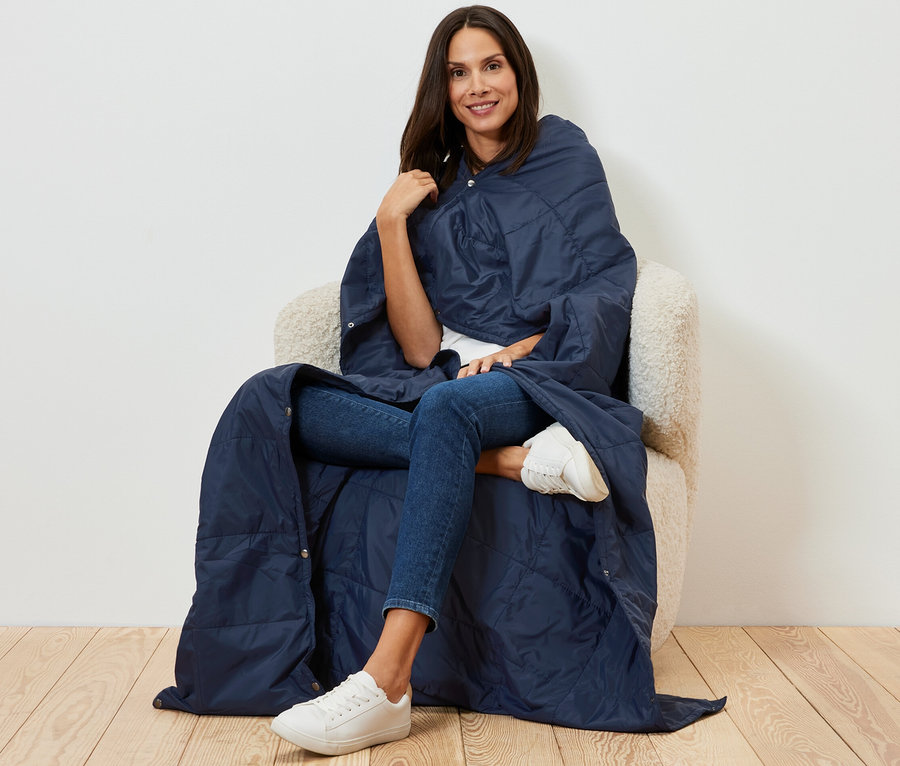 Frau sitzt in Sessel gehüllt in eine ultraleichte Reisedecke.