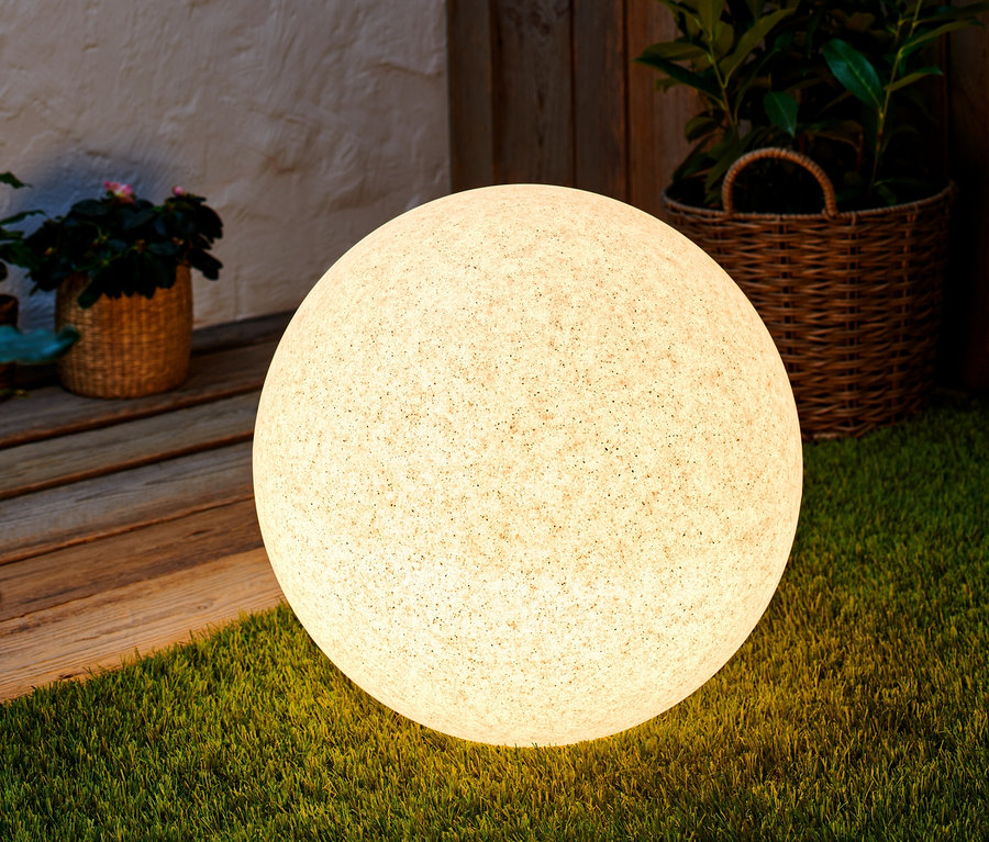 Eine Kugelleuchte mit smartem WiZ-LED-Leuchtmittel steht auf Rasen.