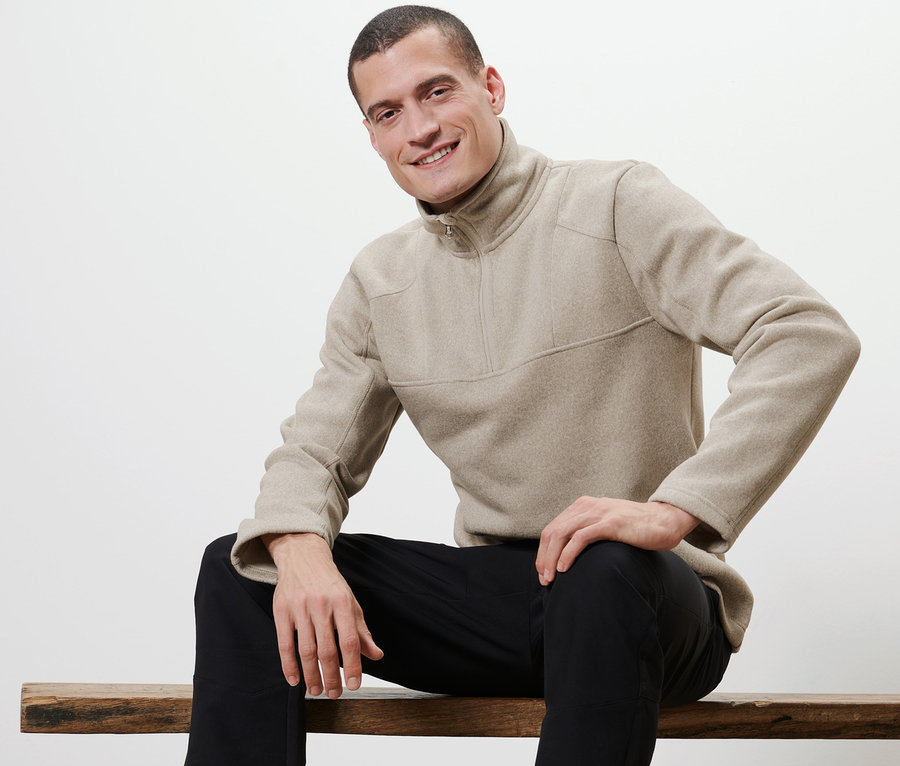 Mann sitzt auf einer Bank und trägt einen Strickfleece-Troyer.