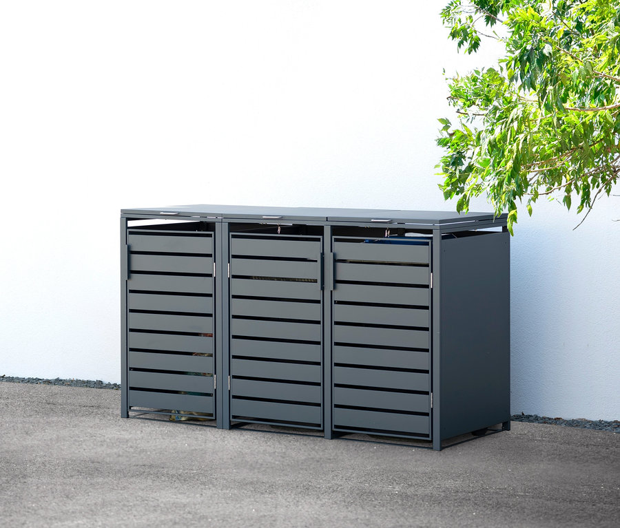 Eine graue Mülltonnenbox aus Stahl für 3 Tonnen steht draußen neben einer weißen Wand.