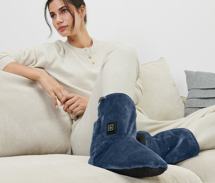 Frau sitzt auf Couch und trägt beheizbare Schuhe.