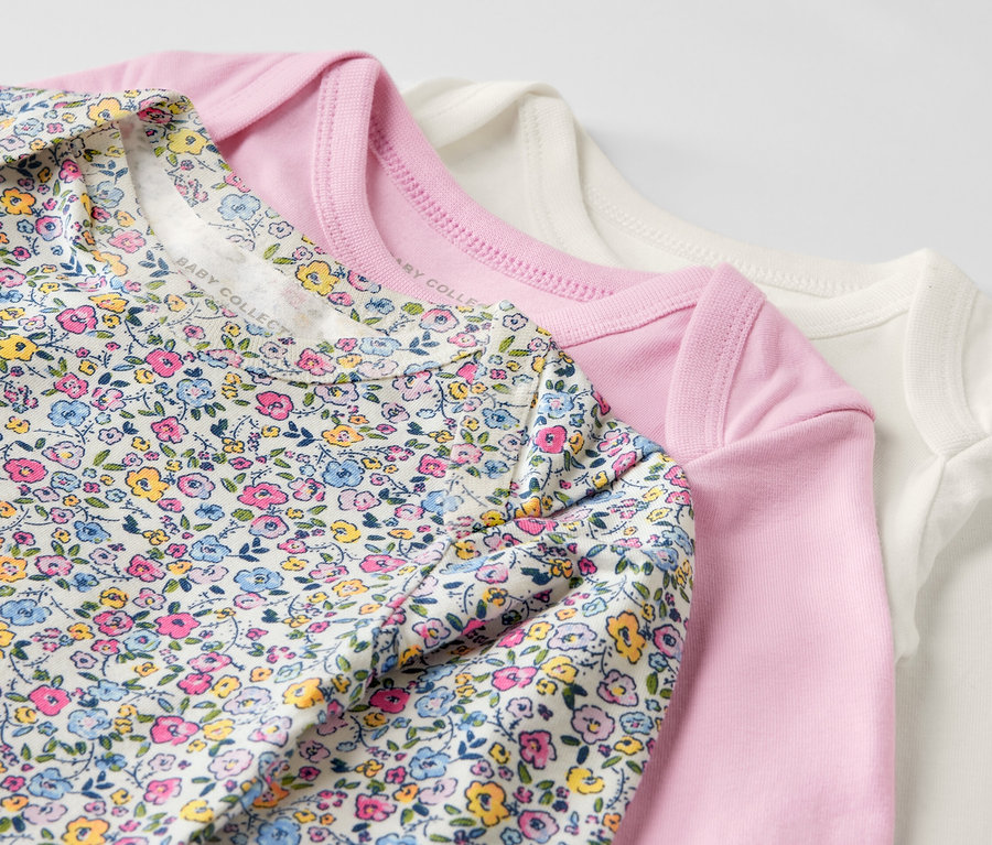 Drei rosa Baby-Bodys mit Mitwachsfunktion liegen übereinander.