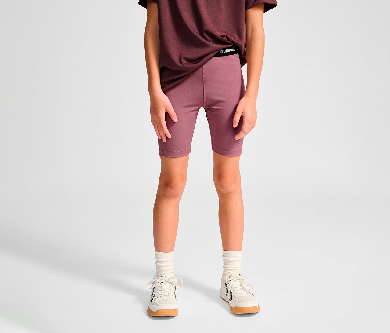 Kind trägt violette HUMMEL HMLJR Pulse MW Short Tight, T-Shirt und Turnschuhe.