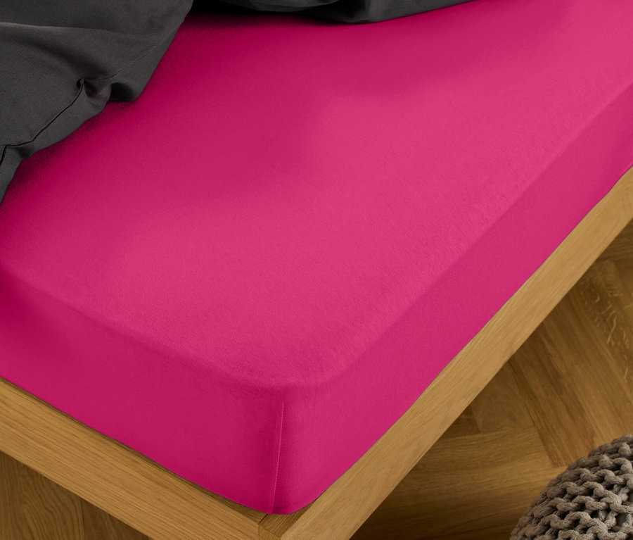 Ein pinkes Jersey-Spannbettlaken in Normalgröße und Doppelgröße auf einem Bett mit einer grauen Decke.