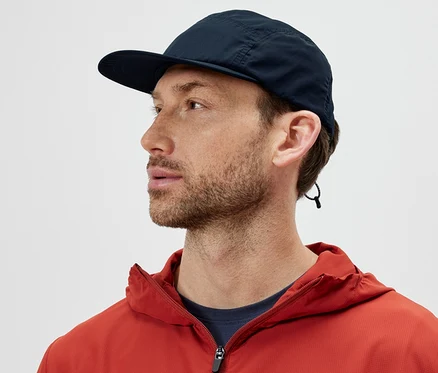 Mann in orangefarbener Jacke trägt ein packbares Cap und schaut nach links.