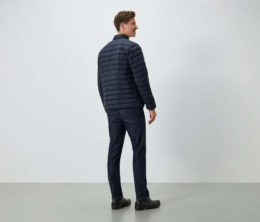 Mann steht mit dem Rücken zur Kamera und trägt eine dunkelblaue Daunenjacke, Jeans und schwarze Schuhe.