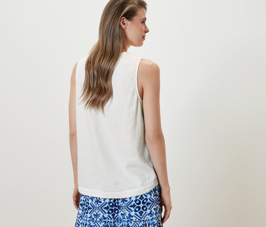Frau trägt eine ärmellose Leinenbluse, weiß, und einen blauen Rock.