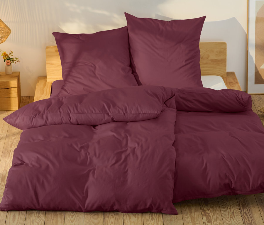 Burgunderfarbene Bettwäsche auf einem Bett mit Holzrahmen.