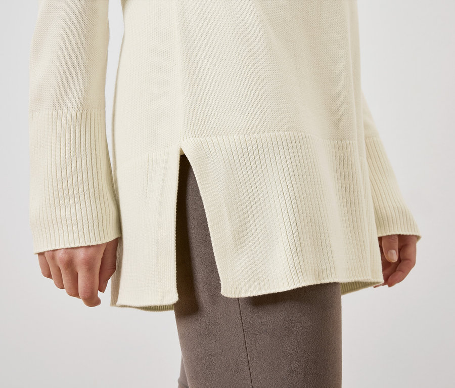 Detailansicht eines langen, cremefarbenen Strickpullovers an einer Frau.