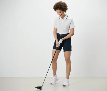 Frau spielt Golf und trägt ein weißes Funktionspoloshirt.