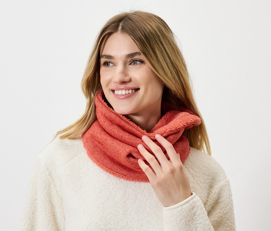 Frau mit blonden Haaren trägt einen korallenroten Loop-Schal und einen cremefarbenen Pullover.
