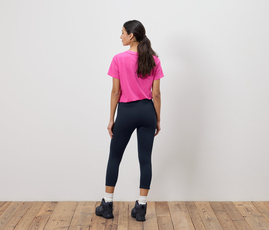 Rückansicht einer Frau mit Pferdeschwanz, die ein pinkes T-Shirt, marineblaue Leggings und schwarze Stiefel trägt.