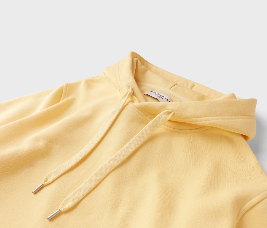 Nahaufnahme eines hellgelben Kapuzenpullovers mit Kordelzug.
