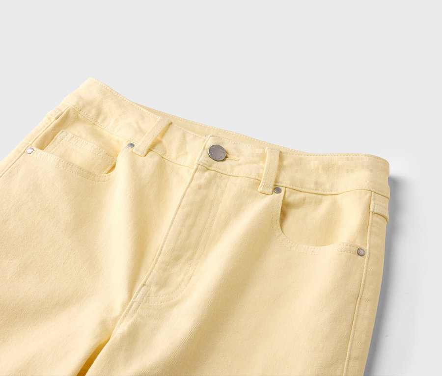 Nahaufnahme einer hellgelben Jeans mit Taschen, Gürtelschlaufen und silberfarbenem Knopf.
