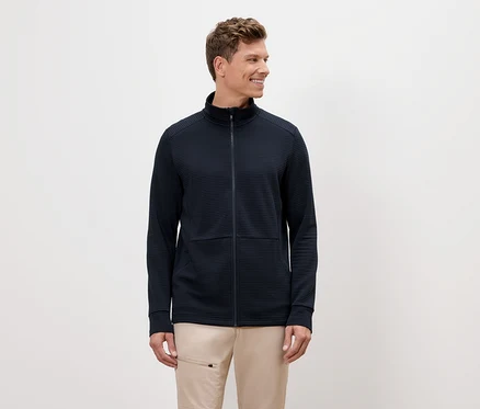 Ein Mann mit blonden Haaren trägt eine marineblaue Reißverschlussjacke und beigefarbene Hosen.