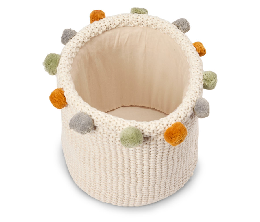 Ein leerer, cremefarbener Strickkorb mit bunten Bommeln.