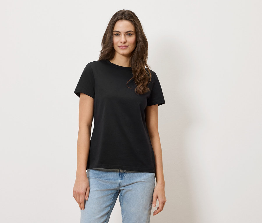 Frau mit gewelltem Haar trägt ein schwarzes T-Shirt und Jeans.