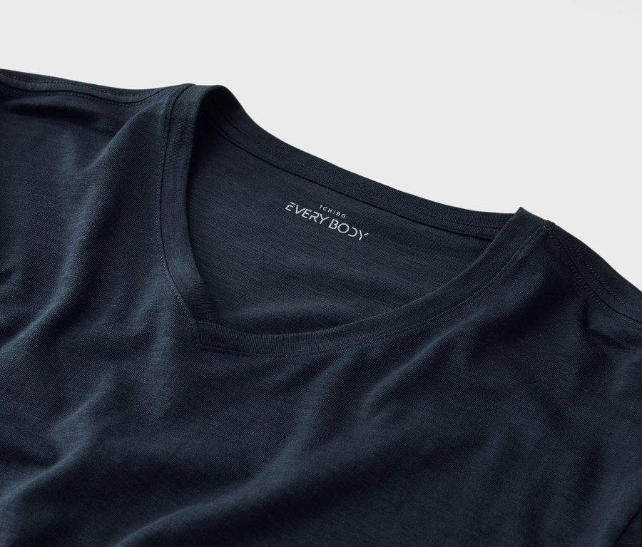 Nahaufnahme eines marineblauen T-Shirts mit V-Ausschnitt und dem Aufdruck "Tchibo EVERY BODY" unterhalb des Kragens.