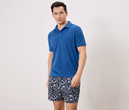 Mann trägt ein blaues Poloshirt und gemusterte Badeshorts.