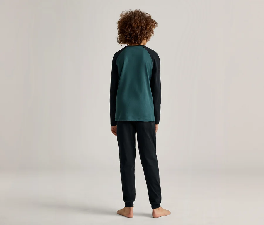 Rückansicht eines barfüßigen Kindes mit lockigem Haar, das einen grün-schwarzen Pyjama trägt.