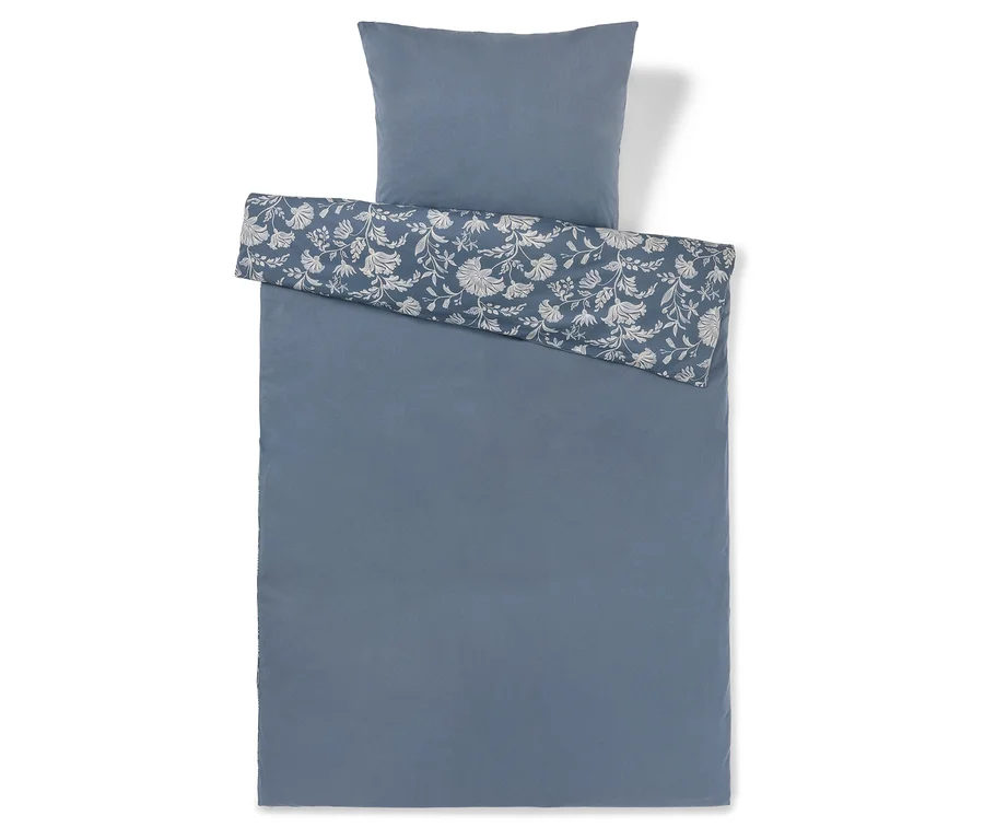 Ein blauer Bettbezug und ein passender Kissenbezug. Der Bettbezug ist größtenteils einfarbig blau, wobei ein umgeschlagener oberer Bereich ein weißes Blumenmuster auf blauem Hintergrund zeigt. Der Kissenbezug ist einfarbig blau.