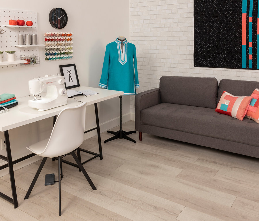 Nähzimmer mit Singer Nähmaschine »M2405« auf weißem Tisch, daneben Stoffstapel und eine Schneiderpuppe mit blauem Kleid.