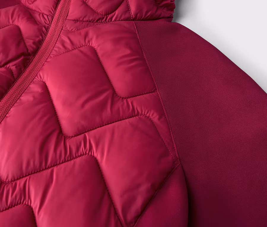 Nahaufnahme einer magentafarbenen Jacke mit gesteppter Vorderseite in geometrischem Muster und glattem Ärmel/Seitenbereich, mit sichtbarem Reißverschluss.